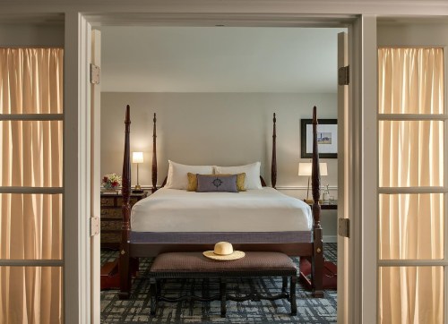 A cozy hotel room featuring a four-poster bed, a bench, and soft lighting through sheer curtains.
