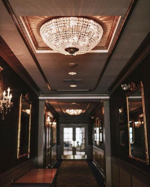A luxurious hallway featuring ornate chandeliers and elegant mirrors, with soft lighting creating a warm ambiance.