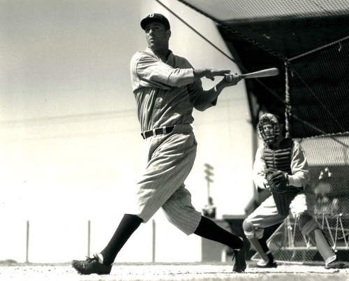 A vintage black-and-white photo of a baseball player swinging a bat, with a catcher in gear behind him.