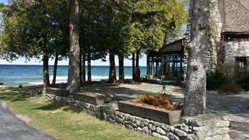 A serene lakeside scene featuring a stone building, trees, and a clear blue sky over calm waters.