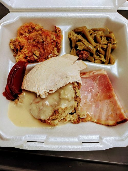 A takeout container with turkey, ham, stuffing, green beans, and sweet potato casserole.