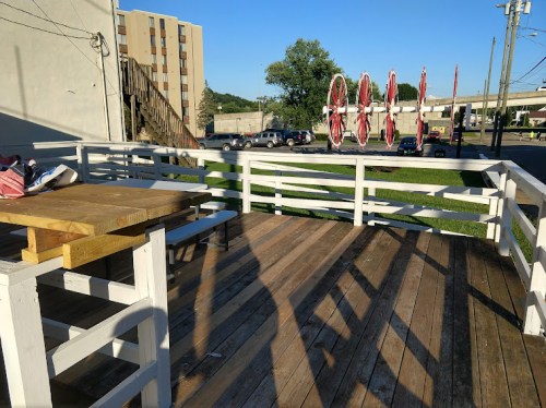 A wooden deck with a table and chairs, overlooking a grassy area and buildings in the background under a clear blue sky.
