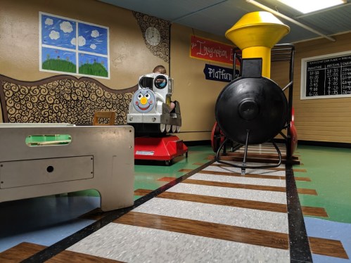 A colorful children's play area featuring a toy train and a train-themed ride-on toy on a track.