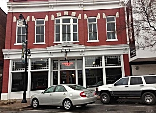 Historic red brick building with large windows, featuring a sign for "Marlinton Place" and parked cars in front.