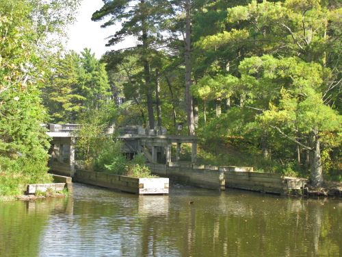 A serene waterway surrounded by trees, featuring a concrete bridge and wooden structures along the banks.