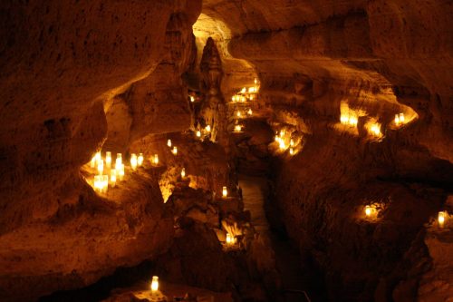 A dimly lit cave with candles illuminating the rocky walls and pathways, creating a warm, mystical atmosphere.
