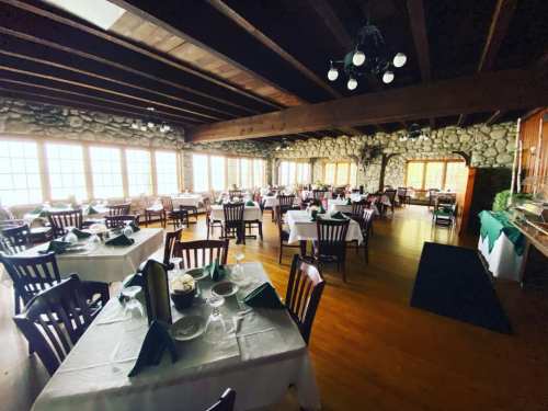 Cozy restaurant interior with stone walls, wooden beams, and neatly set tables with green napkins and white tablecloths.