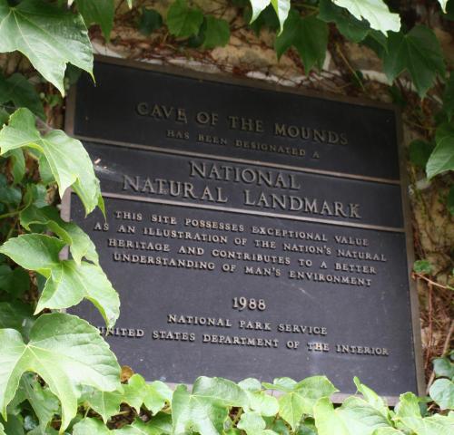 Plaque designating Cave of the Mounds as a National Natural Landmark, surrounded by green foliage.