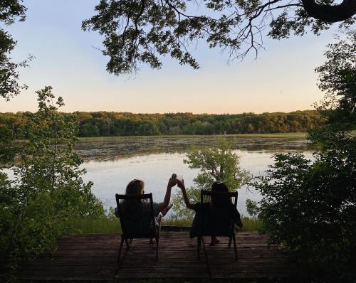 Two people sit on a deck by a serene lake, holding hands and enjoying the peaceful view of the water and trees.