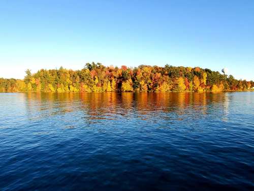 A serene lake scene with an island covered in vibrant autumn foliage under a clear blue sky.