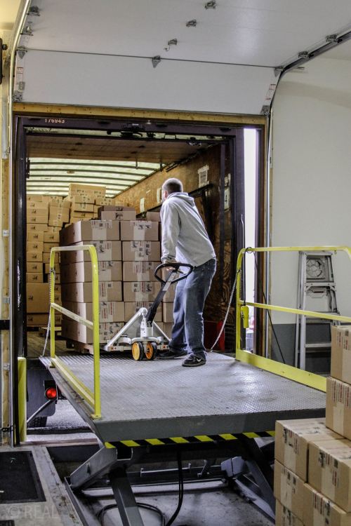 A person using a hand truck to unload boxes from a delivery truck onto a loading dock.