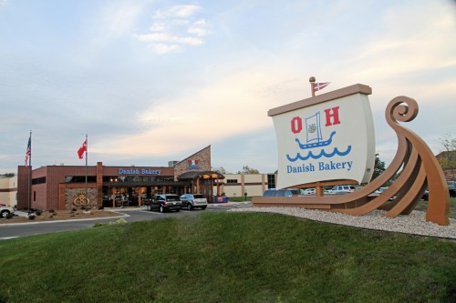 A Danish bakery building with a large sign, flags, and a scenic sky in the background.