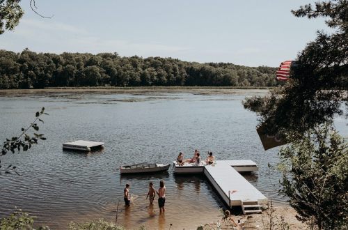 A group of people enjoying a sunny day by a lake, playing near a wooden dock surrounded by trees.