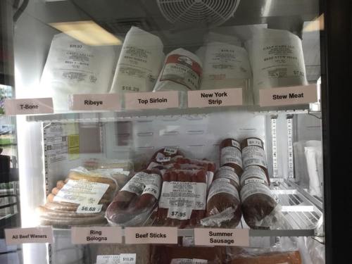 Meat display case with various cuts: T-Bone, Ribeye, Top Sirloin, New York Strip, Stew Meat, and sausages.