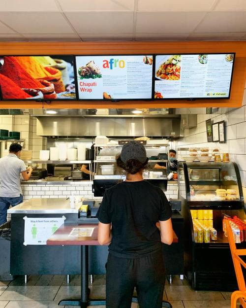 A person stands at a counter looking at a menu board in a restaurant, with food items displayed above.