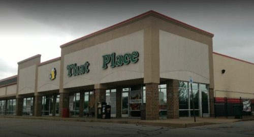 Exterior of a commercial building with a sign reading "That Place" and large windows, under a cloudy sky.