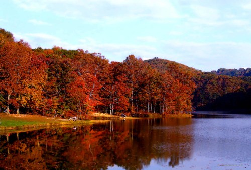 A serene lake surrounded by vibrant autumn trees reflecting in the water under a clear sky.