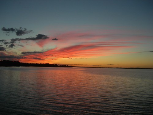 A serene sunset over a calm lake, with vibrant pink and orange clouds reflecting on the water's surface.