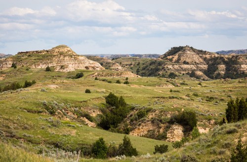 A scenic view of rolling hills and grassy plains under a partly cloudy sky, showcasing natural rock formations.