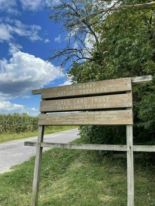 Sign for Kokiwannee Nature Preserve, listing "Acres Land Trust" and open hours from dawn to dusk, surrounded by greenery.