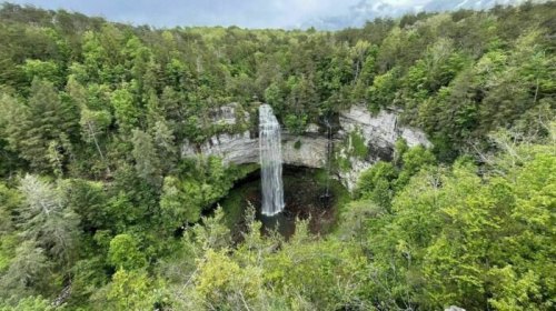 A stunning waterfall cascades down a rocky cliff, surrounded by lush green trees and a serene landscape.