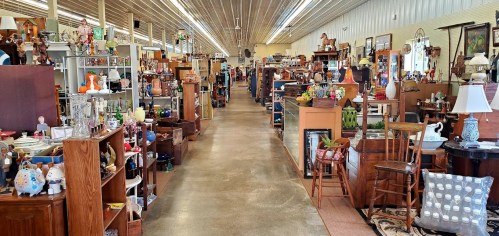 A wide aisle in an antique store filled with various vintage items, furniture, and decor on both sides.