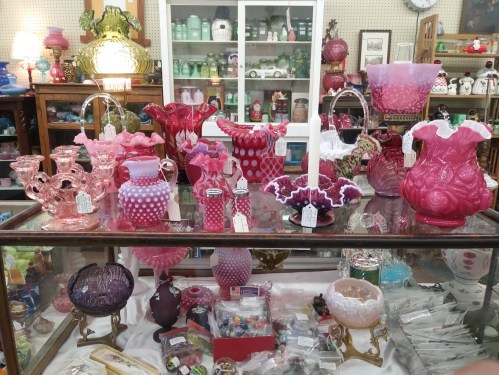 A display of various pink glass vases and decorative items on a glass table in an antique shop.