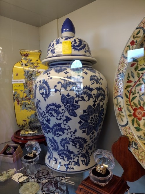 A large blue and white decorative vase with a lid, displayed alongside other ornate pottery and jewelry.