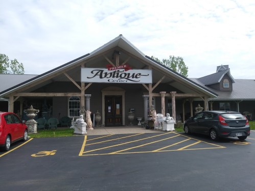A charming antique center with a wooden entrance, surrounded by sculptures and parked cars in front.