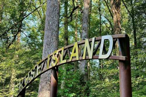 Archway sign reading "Rose Island" surrounded by tall trees and lush greenery.