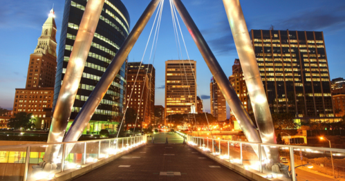 City skyline at dusk, featuring modern buildings and a bridge with illuminated supports.