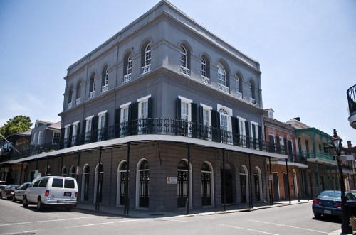 Historic gray building with arched windows and a balcony, located on a sunny street in New Orleans.