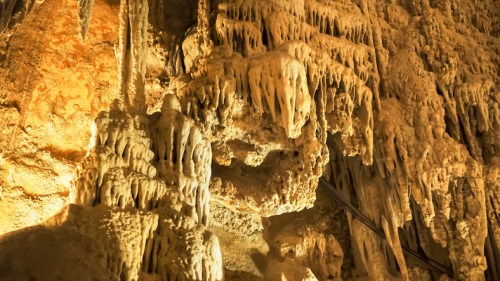 Stalactites and stalagmites in a cave, illuminated with warm lighting, showcasing intricate natural formations.