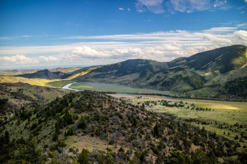 A scenic view of rolling hills and a winding river under a blue sky with scattered clouds.