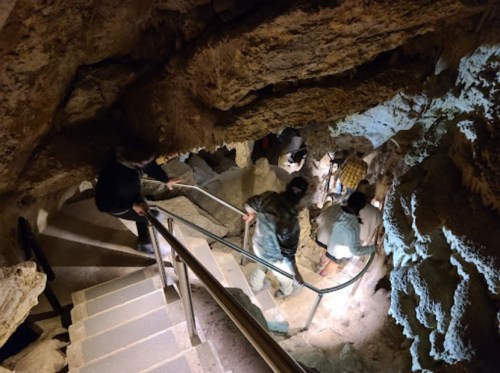 A group of people descends a rocky staircase inside a cave, illuminated by soft lighting.
