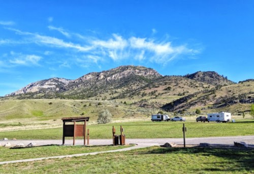 Scenic view of green hills and mountains under a blue sky, with parked RVs in a grassy area.