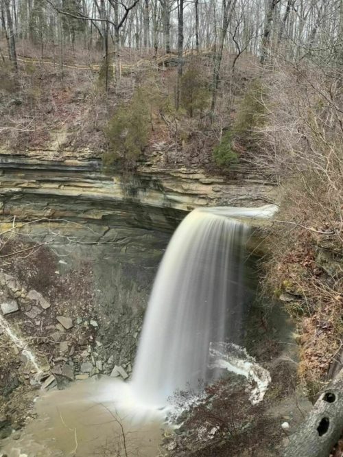 A waterfall cascading over rocky cliffs, surrounded by bare trees and a serene, natural landscape.