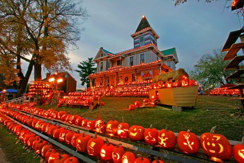 A house decorated with numerous glowing jack-o'-lanterns, creating a festive Halloween atmosphere at dusk.