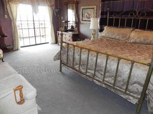 A cozy bedroom featuring a brass bed, floral bedding, and elegant decor with a view of a balcony through glass doors.