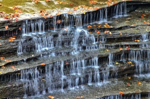 A serene waterfall cascading over layered rocks, surrounded by autumn leaves.