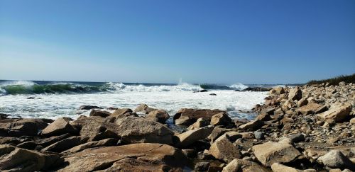 A rocky shoreline with crashing waves under a clear blue sky.