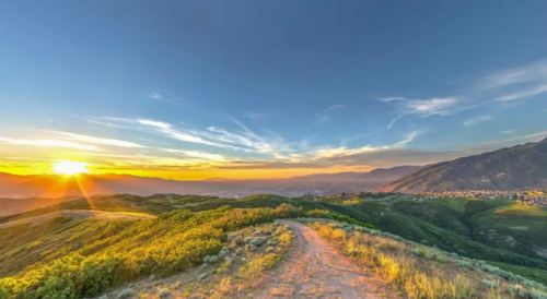 A scenic view of rolling green hills at sunset, with vibrant colors in the sky and a winding path leading into the distance.