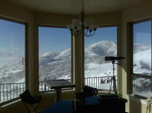 A cozy room with large windows showcasing snowy mountains and a telescope, creating a serene winter view.