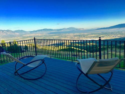 A scenic view from a deck with two chairs overlooking a valley and mountains under a clear blue sky.