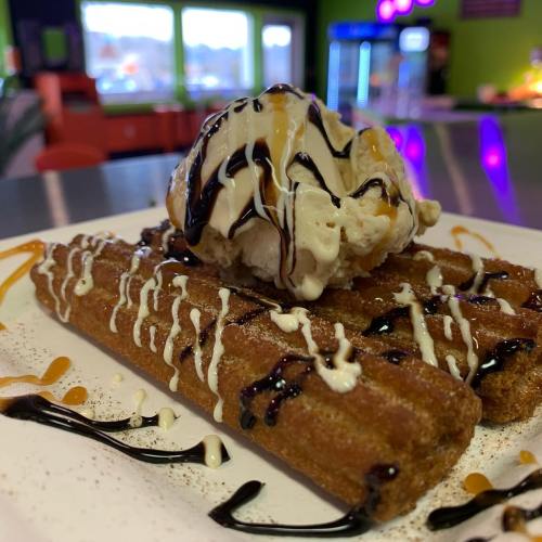 A plate of churros drizzled with chocolate and caramel sauce, topped with a scoop of vanilla ice cream.