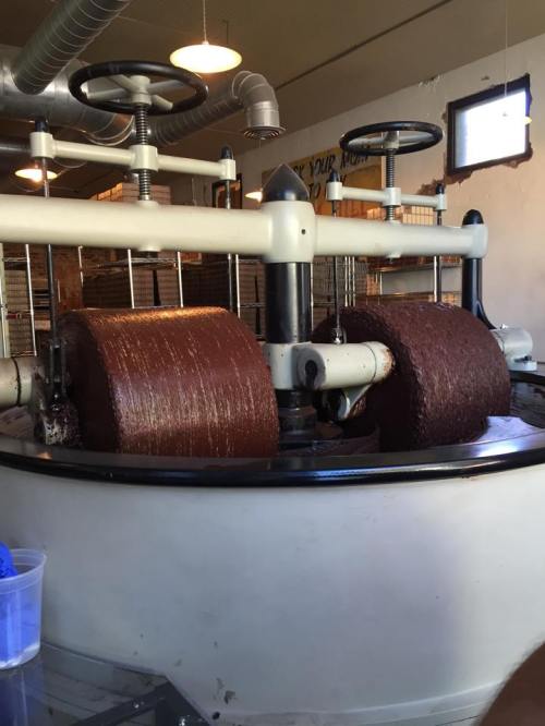 A large machine with two cylindrical rollers covered in brown material, set in a bright, industrial space.