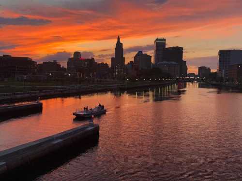 A sunset over a city skyline, reflecting on a calm river with a small boat in the foreground.