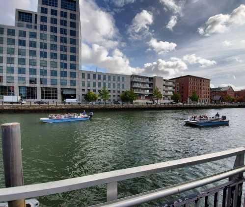 A view of a river with boats, surrounded by modern buildings and a cloudy sky.