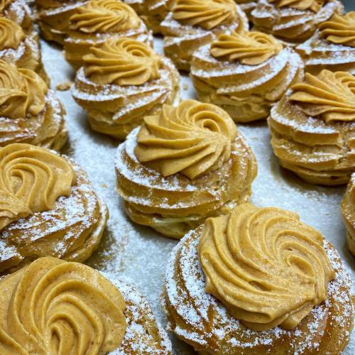 A close-up of cream-filled pastries topped with swirls of frosting and dusted with powdered sugar.