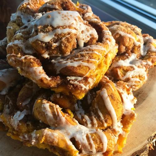 A close-up of a stack of cinnamon rolls drizzled with icing, showcasing a golden-brown, flaky texture.